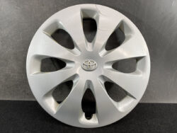 Silver Toyota hubcap with central logo and ten curved spokes, lying on a dark surface