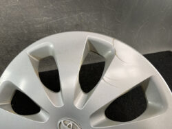 Close-up of a silver alloy wheel rim with visible scratches and cracks, Toyota emblem at the center.