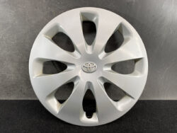 Silver Toyota hubcap with central logo and eight-spoke design, placed against a dark background.