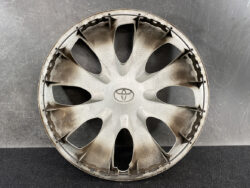 Circular silver Toyota hubcap with multiple spokes, dusty and placed against a dark textured background.