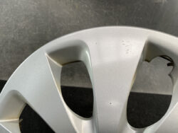 Close-up of a silver car wheel hubcap with chipped paint and a missing section at the edge showing damage on the rim area.