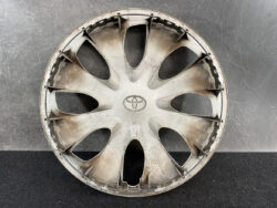 Dusty silver Toyota hubcap with eight curved spokes and central Toyota emblem, resting on a dark surface