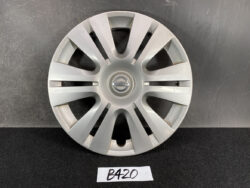 Front view of a silver Nissan hubcap with multiple angled spokes and a central Nissan emblem, placed on a dark surface with a handwritten 'B420' label beneath.