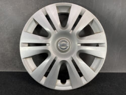 Silver Nissan hubcap with eight split spokes and the Nissan emblem at center mounted on a dark background and floor.