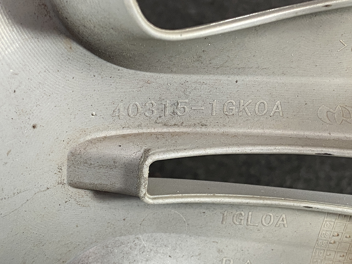 B420_4 NISSAN Genuine 15inch WHEEL CAP / HUB CAP 40315-1GK0A x1 » NZ.95 » JDM-PARTS NZ » JDM-PARTS NZ Close-up of a dusty gray car wheel rim showing the stamped code 40315-1GK0A. NISSAN Genuine 15inch WHEEL CAP / HUB CAP 40315-1GK0A x1 » JDM-PARTS NZ