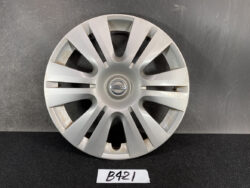 Silver Nissan hubcap with multiple spokes resting on a dark surface; center features Nissan logo in a circular badge (wheel cover)