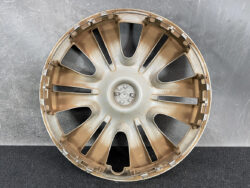 Gold-colored alloy car wheel rim with multiple curved spokes, viewed head-on against a gray background.