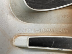 Close-up of a car wheel rim with the stamped part number 40315-1GKOA and a small emblem, dirt and grime on the metal surface.