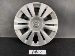 Silver Nissan hubcap with 12 spokes and a central Nissan emblem, resting on a dark surface.