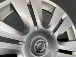 Close-up of a silver Nissan hubcap with scratches and scuffs on the surface around the emblem.