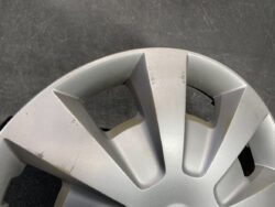 Close-up of a scratched silver car wheel cover with angular spokes and a matte finish.