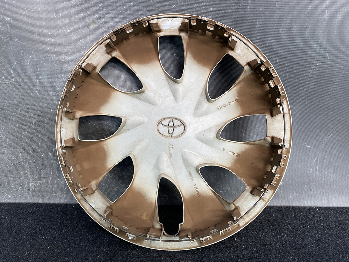 B430_3 TOYOTA PORTE / SPADE Genuine 15inch WHEEL CAP / HUB CAP 42602-52450 x1 » NZ.95 » JDM-PARTS NZ » JDM-PARTS NZ Dirty Toyota hubcap wheel cover with multiple spokes, placed on a dark surface; round, beige-brown plastic with the Toyota emblem in the center TOYOTA PORTE / SPADE Genuine 15inch WHEEL CAP / HUB CAP 42602-52450 x1 » JDM-PARTS NZ