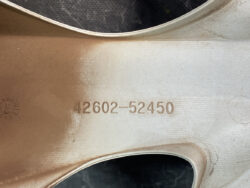 Close-up of a brushed metal surface with the embossed number 42602-52450 and brown dust on the left side.