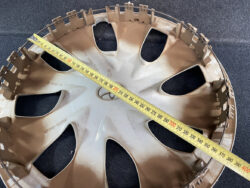 Plastic car hubcap lying on a dark surface with a yellow measuring tape stretched across it, showing about 40 cm in diameter.