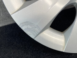 Silver alloy car wheel with curb rash: scraped and scratched paint near the rim edge revealing scuffed layers.