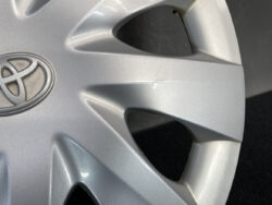 Silver Toyota wheel cover with emblem, showing light scratches along a spoke edge on a dark background.