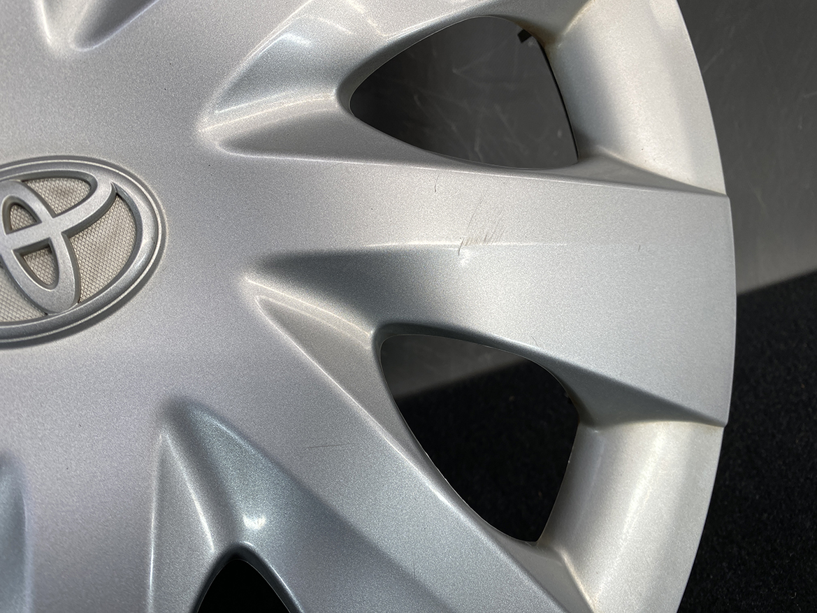 B430_7 TOYOTA PORTE / SPADE Genuine 15inch WHEEL CAP / HUB CAP 42602-52450 x1 » NZ.95 » JDM-PARTS NZ » JDM-PARTS NZ Silver Toyota wheel cover with emblem, showing light scratches along a spoke edge on a dark background. TOYOTA PORTE / SPADE Genuine 15inch WHEEL CAP / HUB CAP 42602-52450 x1 » JDM-PARTS NZ