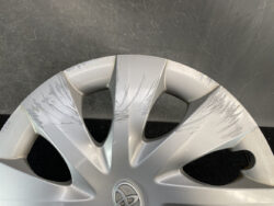 Silver car wheel cover with deep scratches across the spokes and around the rim.