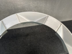 Close-up of a light-gray segmented circular frame with angular, pyramid-like panels on a dark surface.