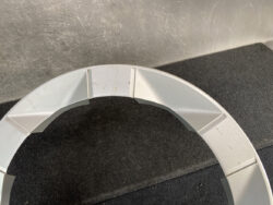 Partial gray circular plastic ring with rectangular internal segments resting on a dark carpet.