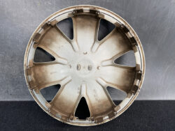 Dusty beige car hubcap with eight curved spokes, placed against a dark background.