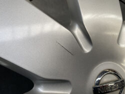 Close-up of a silver Nissan alloy wheel with a long scratch on the surface near the spoke.