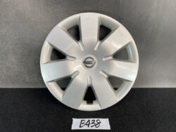Silver Nissan hubcap with an eight-spoke design and center emblem, resting on a dark surface with minor scratches.