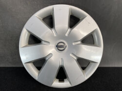 Silver Nissan hubcap with eight spokes and a central Nissan emblem, showing light surface scratches on the rim side trims while resting on a dark backdrop.