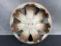 Brown plastic car wheel hubcap with eight spoke-like openings resting on a dark surface, photographed from above.