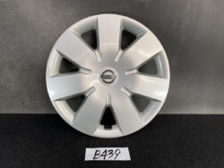 Silver Nissan hubcap laying flat against a dark backdrop, showing the center logo and six spoke-like recesses.
