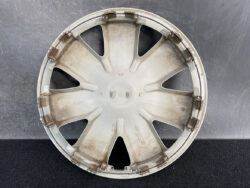 Circular car hubcap with eight spokes, dirty beige color, resting on a dark surface.
