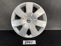 Silver Nissan wheel cover with eight spokes and a central Nissan badge, shown on a dark surface.