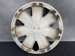 Round gray plastic car hubcap with eight radial spokes and metal rim clips on a dark surface.