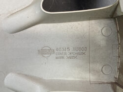 Nissan emblem stamped on a grey metal panel with part number 40315 1U600 and material markings PC+ABS and ABS text beneath it