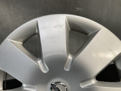 Close-up of a silver car wheel hubcap with several scrapes and scuffs and a Nissan logo at the center.