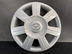 Silver Mazda hubcap wheel cover with eight spokes and Mazda emblem in center, photographed against a dark background.