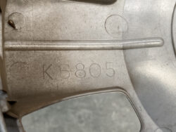 Close-up of a gray metal casting with the engraved serial code K6805 and circular impressions nearby, including a protruding pin.