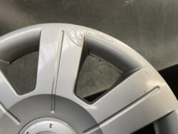 Close-up of a silver alloy car wheel rim with visible scratches and a gouge near a spoke understood as damage to the rim edge .