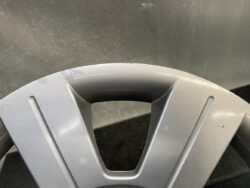 Close-up of a gray plastic car wheel cover with three spokes and a central triangular opening, showing a few scratches.