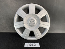 Silver Mazda hubcap with central Mazda logo against a dark backdrop on a black surface.