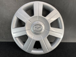 Silver Mazda hubcap with a centered logo and eight radial spokes on a dark background