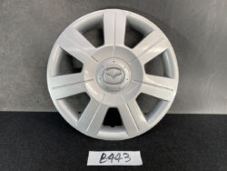Silver Mazda hubcap with eight-spoke design and centered logo on a dark surface