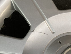 Close-up of a silver alloy car wheel with a deep scratch and small chips along the rim edge.