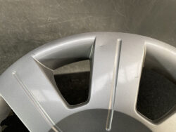 Close-up of a silver car wheel cover with three broad spokes and triangular openings on a dark background.