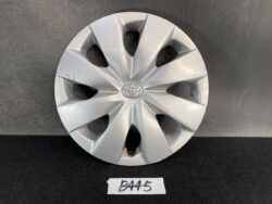 Silver Toyota wheel hubcap with central emblem, resting against a dark backdrop with visible scratches on the rim.