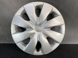 Silver Toyota wheel hubcap with a cracked/scuffed edge and light rust along the bottom, circular wheel cover with a central Toyota emblem behind spokes.