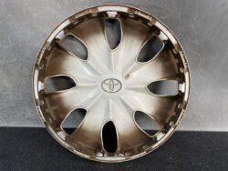 Round beige Toyota hubcap with an eight-spoke design and central Toyota emblem, resting on a dark surface.