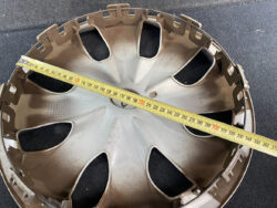 Brown plastic car wheel hubcap laid on a dark surface with a yellow tape measure stretched across its diameter.