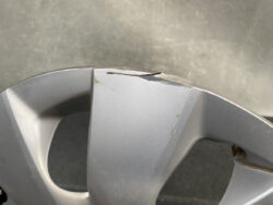 Cracked and chipped silver alloy car wheel rim with visible surface damage along the edge.