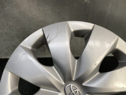 Silver car wheel hubcap with a Toyota emblem showing multiple scratches and scuffs on the surface.